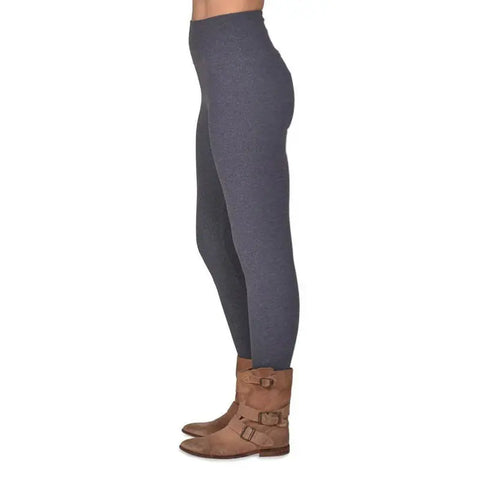 Shown from the waist down against a white background, a person stands in profile wearing Spiritex | Sustainable Apparel Yoga Leggings | 45/45/10 Charcoal paired with brown ankle boots with buckles.