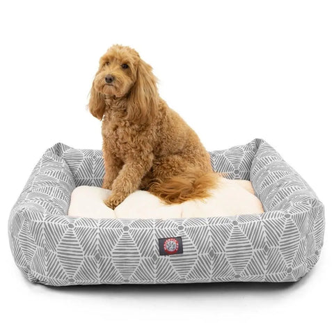 A fluffy, light brown dog lounges on the Charlie Luxe Bagel Bed by Majestic Pet, featuring gray and white patterns, raised sides, and a cream cushion for comfort and style—all in a machine washable design.