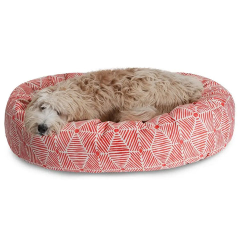 A fluffy, light-colored dog is relaxing on the Majestic Pet Charlie Sherpa Bagel Dog Bed, resting its head on the edge and looking comfortable.