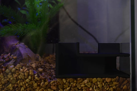 The Chatelet Aquarium Underground Tunnel by Chatelet Manufacturing is featured on the right, set in a tank with brown gravel, a plastic plant on the left, and some visible aquarium wiring in the background.