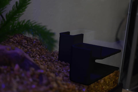 The Chatelet Aquarium Underground Tunnel by Chatelet Manufacturing sits on brown gravel in a fish tank, with a green artificial plant to the left and a white wall behind. Perfect hideout for fish and shrimp; made in the USA.