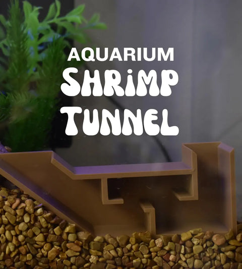 The Chatelet Aquarium Underground Tunnel by Chatelet Manufacturing sits on gravel with green plants behind, creating ideal decor and a hideout for shrimp and fish. Text above reads: Chatelet Aquarium Shrimp Tunnel. Made in USA.