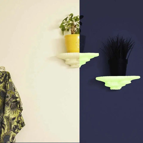 A wall split in half: the left side has a yellow shelf with a yellow pot and plant, plus a vibrant patterned cloth; the right side showcases Chatelet Mushroom Floating Shelves by Chatelet Manufacturing, each holding black pots with plants.