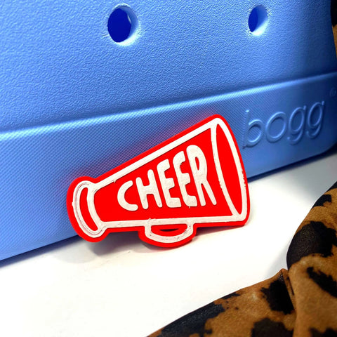 The Chatelet Manufacturing BOGLETS Cheerleading Charm (Red Megaphone) is attached to a light blue Bogg Bag with a touch of leopard-print fabric, adding school spirit and style to your tote.
