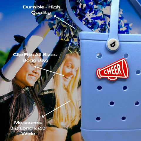 Close-up of a blue Bogg Bag with a red Chatelet Manufacturing BOGLETS Cheerleading Charm (Red Megaphone) attached. Labeled features highlight its durability, secure clip fit, and perfect size for tote bag decoration. Smiling cheerleaders appear in the background.