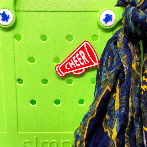 The BOGLETS Cheerleading Charm (Red Megaphone) by Chatelet Manufacturing is shown attached to a bright green Bogg Bag, with a blue and yellow scarf draped on the right side.