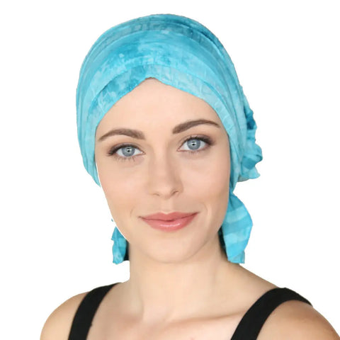 A woman with light skin and blue eyes wears the bright blue Molly Chemo Beanies® scarf by Chemo Beanies®, paired with a black tank top. She smiles softly at the camera against a white background.