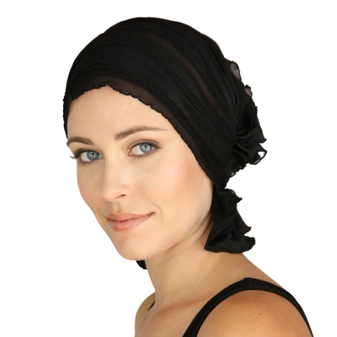 A light-skinned woman with blue eyes wears the Chemo Beanies® Angelle scarf in black, gazing slightly to the side with a gentle smile.