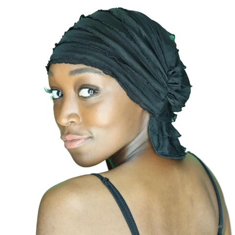 A woman wearing the Chemo Beanies® Angelle black chemo head cover and a black sleeveless top looks over her shoulder with a slight smile against a white background.
