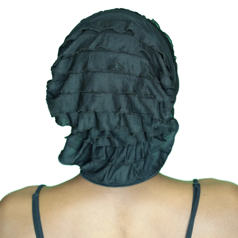 A person seen from behind wears the Chemo Beanies® Angelle scarf by Chemo Beanies®—a black, ruffled head covering—with a black spaghetti strap top and visible shoulders.