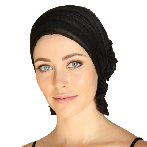 A light-skinned woman with blue eyes and subtle makeup wears the Chemo Beanies® Angelle black slip-on beanie and a black top, facing the camera with a neutral expression.