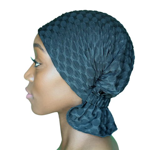 A woman in profile wears the textured, black Chemo Beanies® - Emma by Chemo Beanies®, covering her head and hair. The plain background highlights this stylish cancer headwear option.
