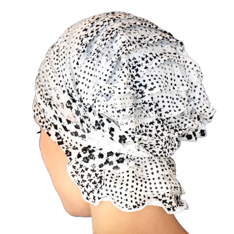A person wearing the Chemo Beanies® - Reagan, a white headscarf with black polka dots and floral patterns, photographed from behind against a white background—ideal stylish chemo head cover by Chemo Beanies®.