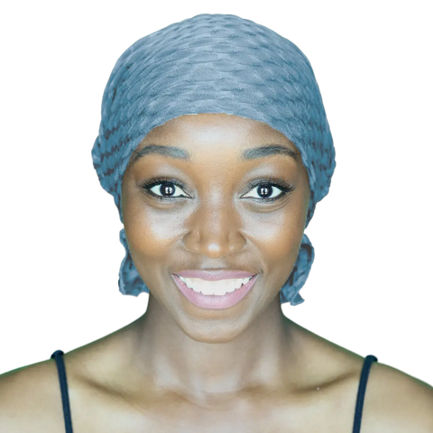 A dark-skinned woman smiles brightly, wearing the Chemo Beanies® Zoe textured grey scarf and a black strap top, set against a plain white background.