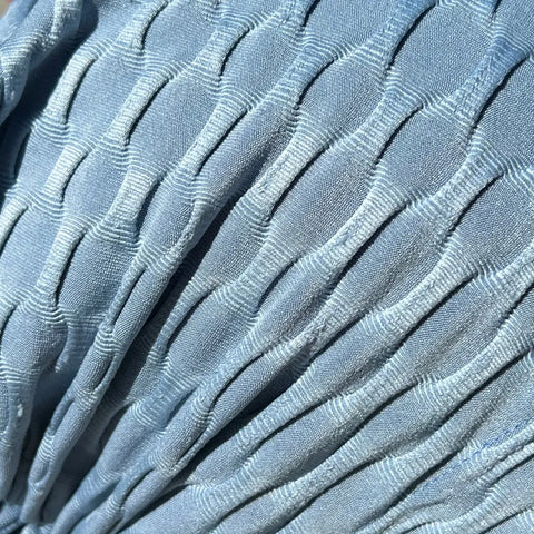 Close-up of the Zoe Chemo Beanies® scarf by Chemo Beanies®, made from light blue, pleated fabric with vertical ridges. Intricate weave catches sunlight—ideal for slip-on beanies and comfortable cancer headwear like chemo beanies.