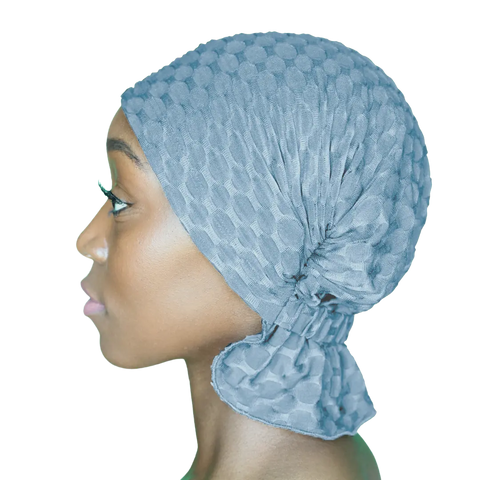 A woman in profile wears the Zoe Chemo Beanies® by Chemo Beanies®, a textured light blue chemo beanie that covers her hair and ties at the back, against a plain white background.