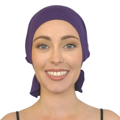 A smiling woman faces forward against a plain background, wearing a Violet Chemo Beanies® slip-on beanie and a black top.