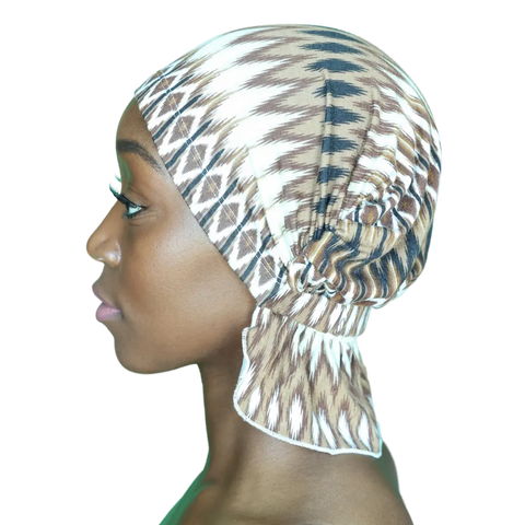 A woman in profile wears the Chemo Beanies® Scarves - Roberta, a stylish chemo head cover with brown, white, and black geometric patterns. It is tied at the back and fully covers her hair. Background is transparent.