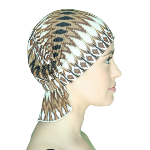 A woman in profile wears the Chemo Beanies® Roberta slip-on beanie with brown, black, and white geometric patterns. The gathered back covers her hair fully. The plain background keeps focus on the Scarves - Chemo Beanies® product.