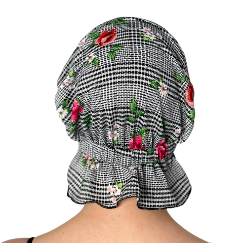 A person is seen from behind wearing the Chemo Beanies® Pixie chemo beanie, featuring black-and-white checks with red, pink, and white floral patterns, set against a black background.