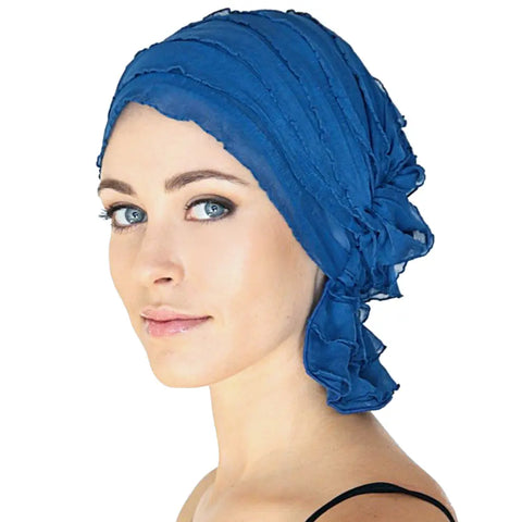 A woman with light skin and blue eyes models the Chemo Beanies® Muriel, a sheer textured royal blue chemo head cover, looking neutrally at the camera against a white background.
