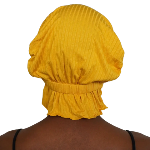 A person wears the Chemo Beanies® Martha—a yellow textured slip-on beanie with ruffled edges—seen from behind against a plain background. Their black top straps are visible, showcasing this stylish scarf for chemo patients.