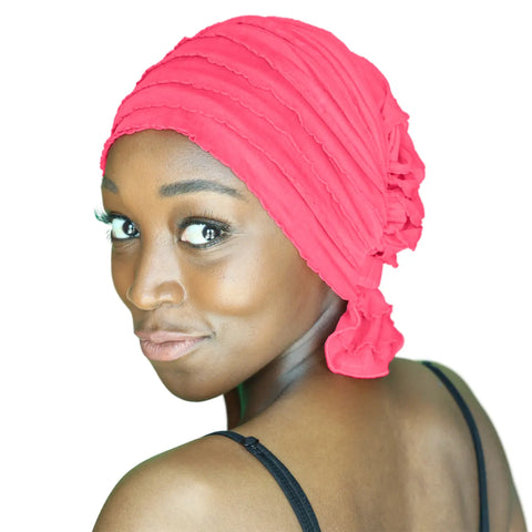 A woman with dark skin wears the Chemo Beanies® Carol scarf by Chemo Beanies®. She looks over her shoulder and smiles slightly, dressed in a black top with long eyelashes, set against a white background.