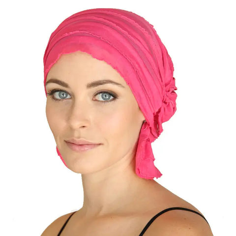 A woman with light skin and blue eyes wears the bright pink Carol Chemo Beanie® by Chemo Beanies®, looking at the camera with a neutral expression against a plain white background.