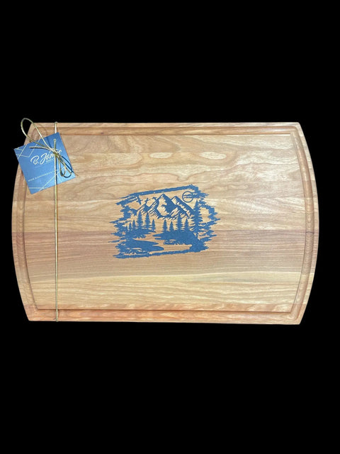 The Blue Steel Epoxy Inlay Cherry Serving Tray by B. James Design & Woodwork features handcrafted artistry, with a dark blue steel epoxy mountain and river design, grooved outer edge, gold-tied gift tag, and a solid black background.