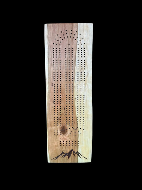 The Cherry Live Edge Cribbage Board With Mountain Engraving by B. James Design & Woodwork features three columns of peg holes, a stunning mountain engraving at the bottom, and is crafted from solid cherry wood.