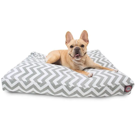 A light brown French Bulldog relaxes on the Majestic Pet Chevron Rectangle Dog Bed, featuring a gray and white chevron pattern and a removable cover, looking forward with its ears up and mouth slightly open.