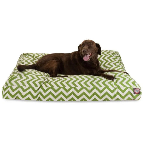 A brown dog lies on the Majestic Pet Chevron Rectangle Dog Bed, featuring a green and white chevron pattern, looking at the camera with its tongue out.