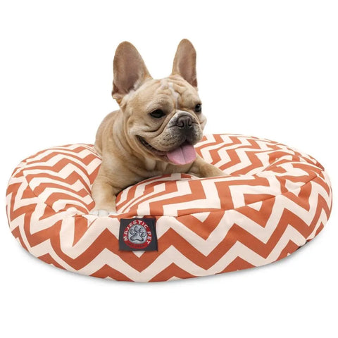 A light brown French Bulldog lies happily on the Majestic Pet Chevron Round Dog Bed, which has an orange and white zigzag pattern and a removable, washable cover for easy cleaning.