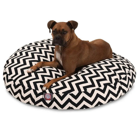 A brown dog with a white chest lies on the Majestic Pet Chevron Round Dog Bed, featuring a black and white zigzag pattern, washable material, and removable cover against a white background.