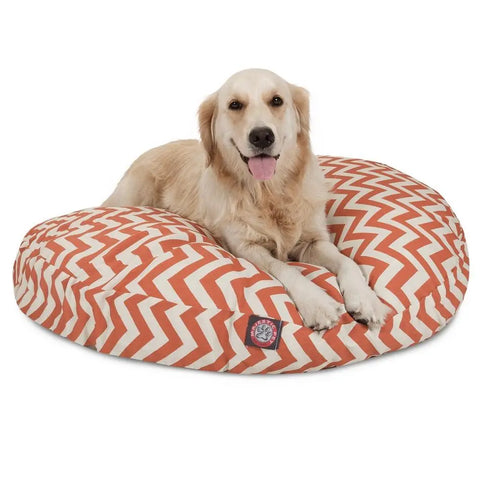 A golden retriever rests happily with its tongue out on the Majestic Pet Chevron Round Dog Bed, which has an orange and white chevron pattern and a washable, removable cover for easy cleaning.