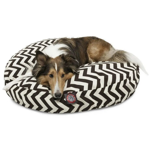 A dog with long brown, white, and black fur lies on the Majestic Pet Chevron Round Dog Bed, featuring a black and white zigzag pattern, resting its head on the cozy, washable bed.