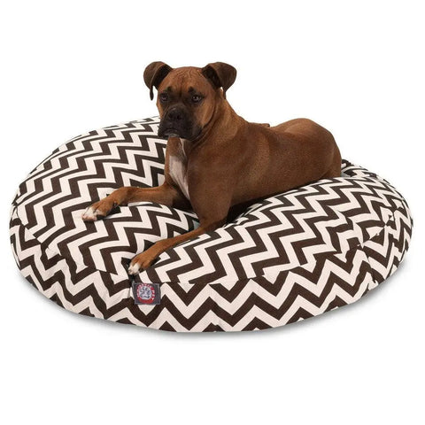 A brown dog with a white chest is lying on the Majestic Pet Chevron Round Dog Bed, featuring a black-and-white zigzag pattern and a removable washable cover, against a plain white background.