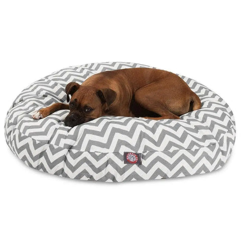 A brown dog rests on the Majestic Pet Chevron Round Dog Bed, which has a gray and white chevron design and a removable cover for easy cleaning.