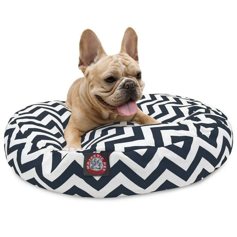 A tan French Bulldog relaxes on the Majestic Pet Chevron Round Dog Bed, featuring a black and white zigzag pattern and a washable cover. A small label with a paw print logo is visible on the front.