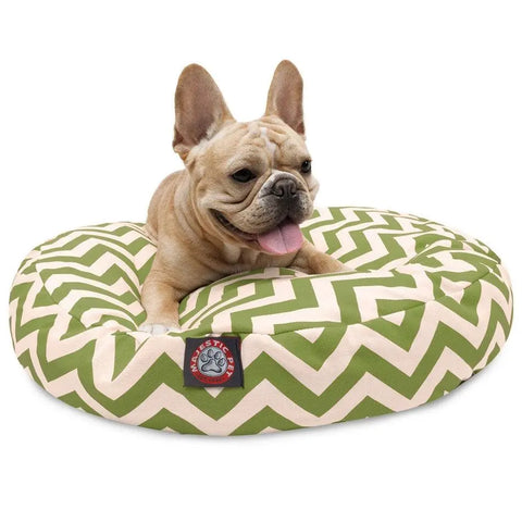 A light brown French Bulldog rests happily with its tongue out on the Chevron Round Dog Bed by Majestic Pet, featuring a green and white zigzag pattern, washable removable cover, and a Majestic Pet logo on the front.