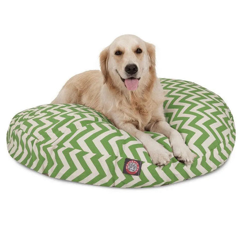 A golden retriever relaxes on the Majestic Pet Chevron Round Dog Bed, featuring a green and white zigzag pattern, looking at the camera with its tongue out.