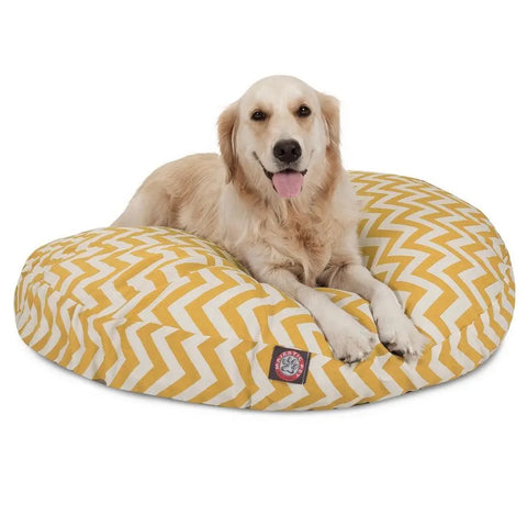 A golden retriever relaxes on the Majestic Pet Chevron Round Dog Bed, featuring a washable yellow and white zigzag pattern, looking content with its tongue out.