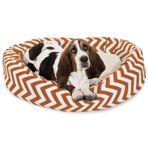 A black and white basset hound relaxes on the Majestic Pet Chevron Sherpa Bagel Dog Bed, featuring a round, orange and white chevron design made from outdoor-treated polyester.