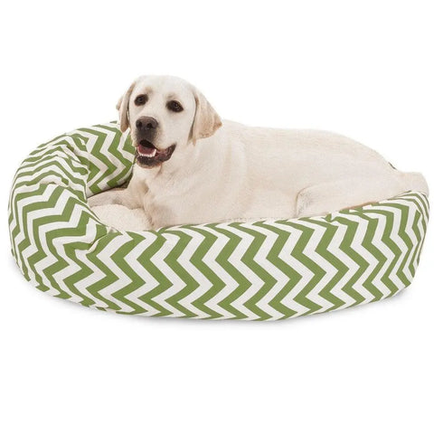 A light-colored Labrador retriever is lying relaxed in the Majestic Pet Chevron Sherpa Bagel Dog Bed, featuring a green and white zigzag pattern and made from outdoor treated polyester.