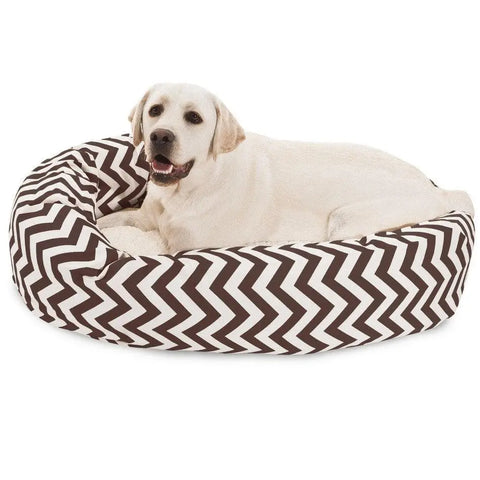 A yellow Labrador lounges on the Majestic Pet Chevron Sherpa Bagel Dog Bed, featuring a brown and white zigzag pattern, outdoor-treated polyester for water resistance, and spine support for extra comfort.