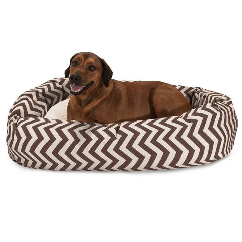 A brown dog relaxes on the Majestic Pet Chevron Sherpa Bagel Dog Bed, featuring a brown and white zigzag design. Made with outdoor-treated polyester, this bed offers durability and comfort as the dog faces forward with its mouth slightly open.