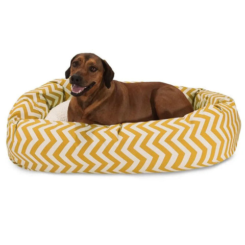 A brown dog is relaxing in the Majestic Pet Chevron Sherpa Bagel Dog Bed, featuring a yellow and white chevron pattern and water-resistant fabric.