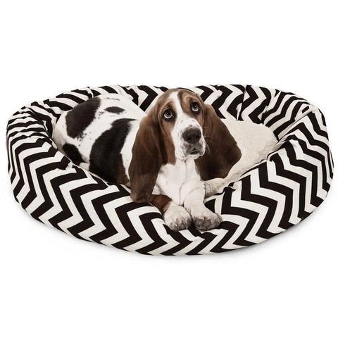 A basset hound with brown and white fur relaxes in the Majestic Pet Chevron Sherpa Bagel Dog Bed, which features a water-resistant fabric and a black-and-white zigzag pattern.