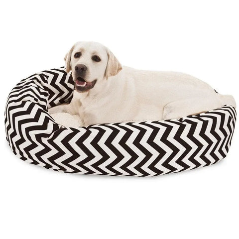 A light-colored Labrador retriever relaxes on the Majestic Pet Chevron Sherpa Bagel Dog Bed, featuring a black and white zigzag pattern and water-resistant, outdoor-treated polyester.