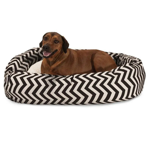 A brown dog is lying in the Chevron Sherpa Bagel Dog Bed by Majestic Pet, featuring a black and white zigzag pattern and made from water-resistant, outdoor-treated polyester.